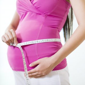 Young pregnant woman measuring waistline